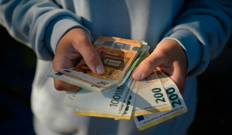 Person in hellblauem Pullover hält mehrere Euro-Banknoten in den Händen, darunter 50-, 100- und 200-Euro-Scheine.