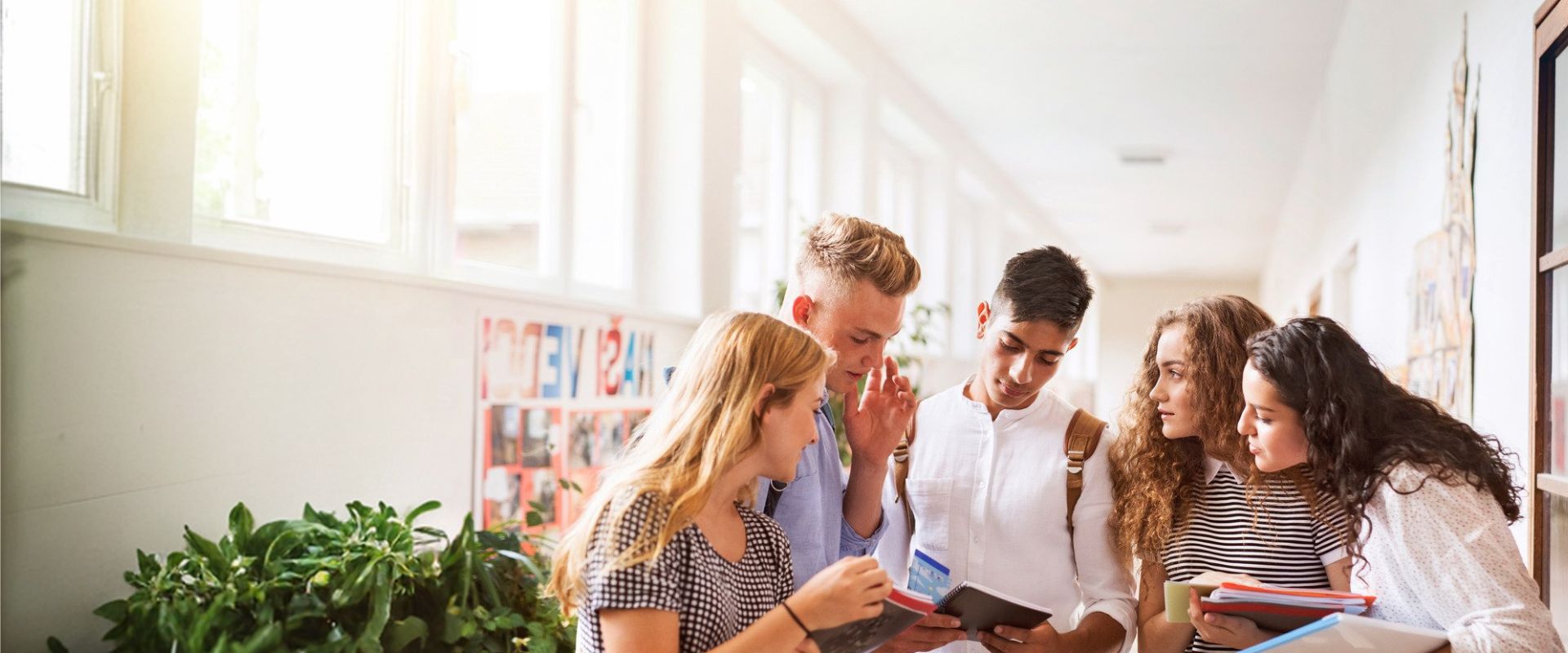 Fünf Jugendliche stehen im Flur und schauen gemeinsam in ein Notizbuch, einige halten Hefte und Bücher.