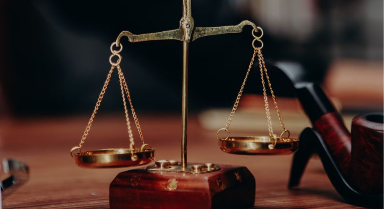 Eine goldene Waage steht auf einem Holztisch – Symbol für Gerechtigkeit und Gleichgewicht. Im Hintergrund sind unscharf weitere Gegenstände zu erkennen.