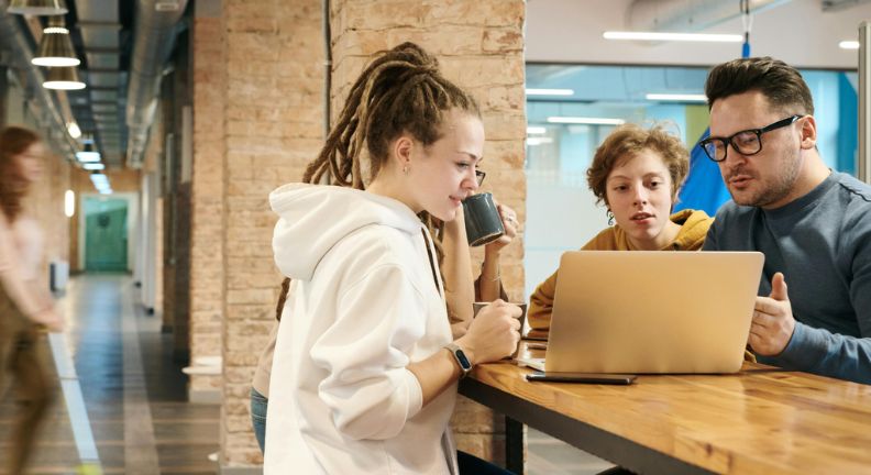 Eine Gruppe von Mitarbeitenden steht um einen Laptop herum. Das Büro hat einen rustikalen und modernen Charme.